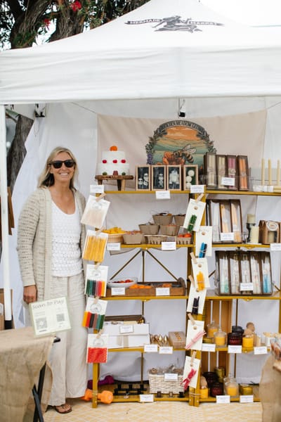 A candle maker beside her shelf under the Mermade tent
