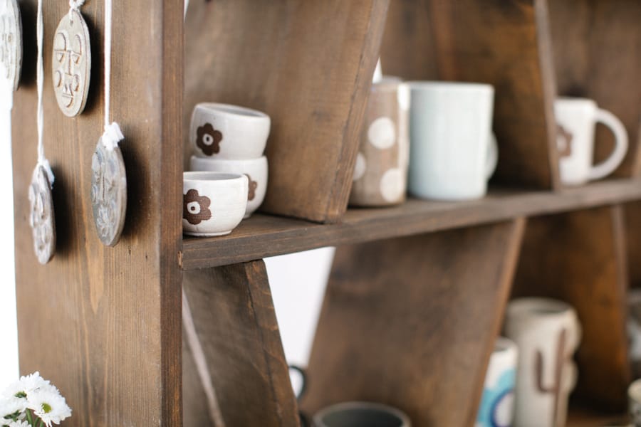 Handmade mugs and hanging ornaments on a walnut shelf
